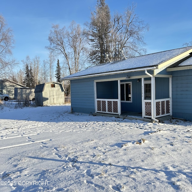 snow covered rear of property featuring a shed