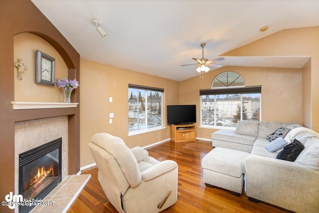 living room with a tile fireplace, hardwood / wood-style flooring, ceiling fan, and vaulted ceiling