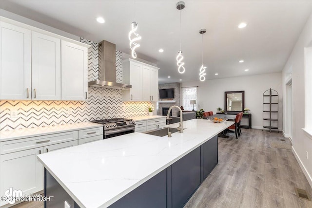 kitchen with a sink, visible vents, white cabinets, wall chimney range hood, and stainless steel range with gas stovetop