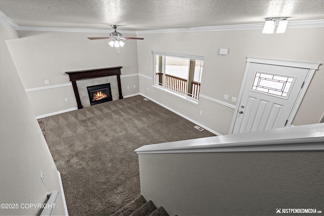 unfurnished living room featuring a tiled fireplace, crown molding, a textured ceiling, and carpet flooring