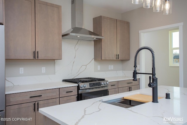 kitchen featuring light stone countertops, wall chimney range hood, stainless steel range with gas stovetop, and sink