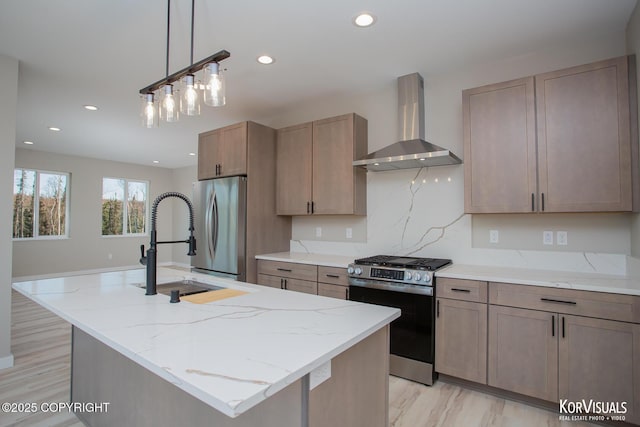 kitchen with stainless steel appliances, a kitchen island with sink, wall chimney exhaust hood, and sink