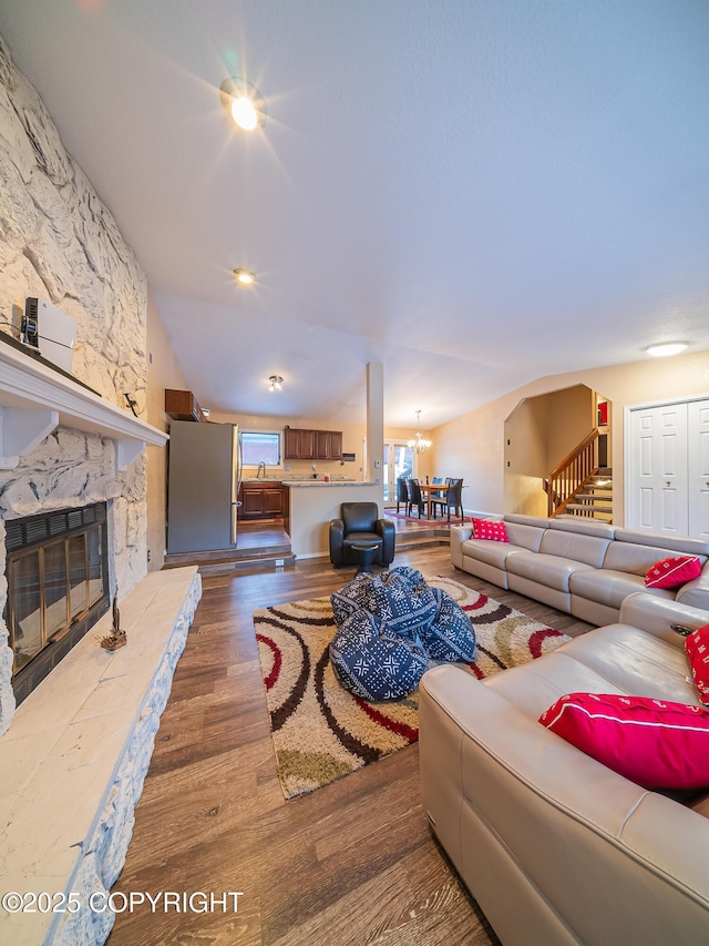 living room with hardwood / wood-style flooring, a stone fireplace, and a chandelier