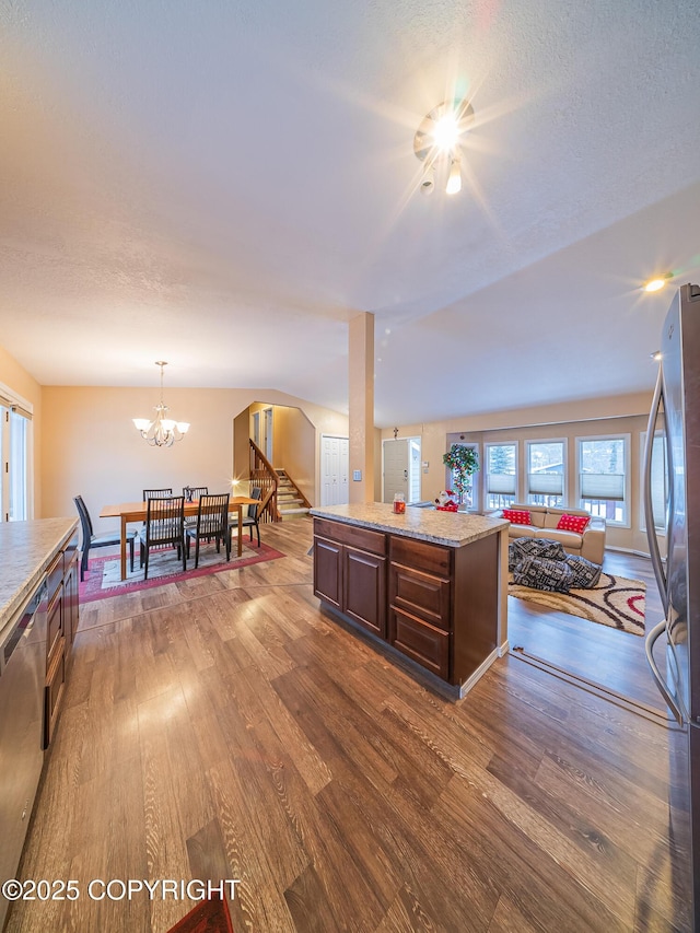 kitchen with appliances with stainless steel finishes, pendant lighting, hardwood / wood-style flooring, a center island, and an inviting chandelier