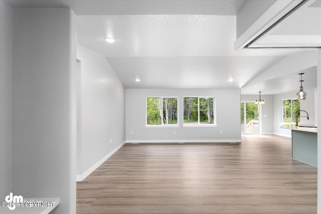 unfurnished living room with light wood-type flooring, a healthy amount of sunlight, vaulted ceiling, and a notable chandelier