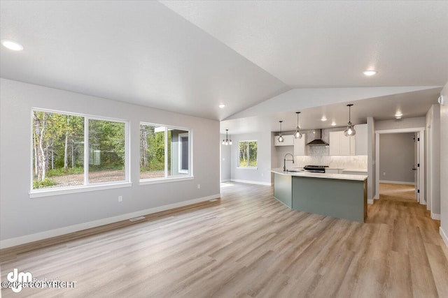 kitchen featuring sink, decorative light fixtures, lofted ceiling, wall chimney range hood, and a kitchen island with sink