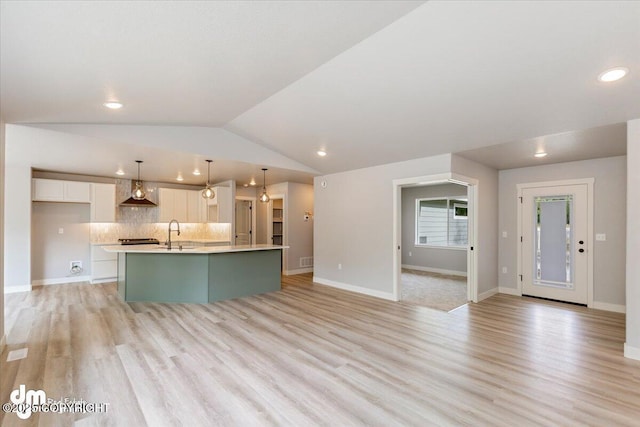 kitchen with white cabinets, a center island with sink, light hardwood / wood-style flooring, and pendant lighting