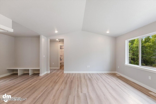 empty room with a textured ceiling, vaulted ceiling, and light hardwood / wood-style flooring