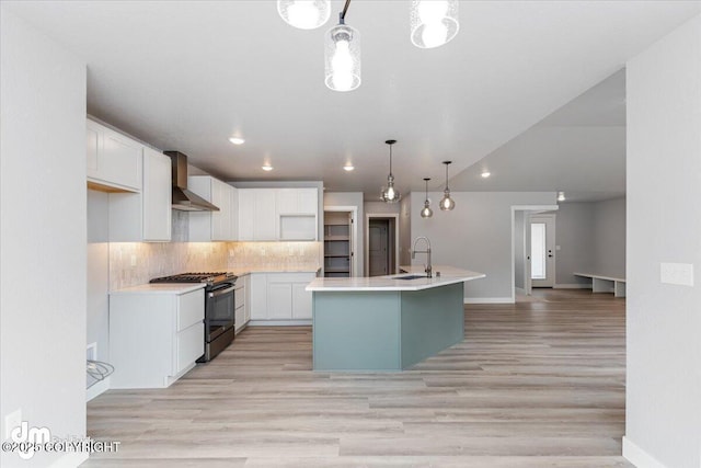 kitchen featuring a center island with sink, hanging light fixtures, wall chimney exhaust hood, white cabinets, and stainless steel range oven