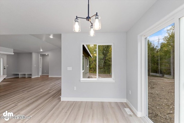 unfurnished dining area with an inviting chandelier and light hardwood / wood-style flooring