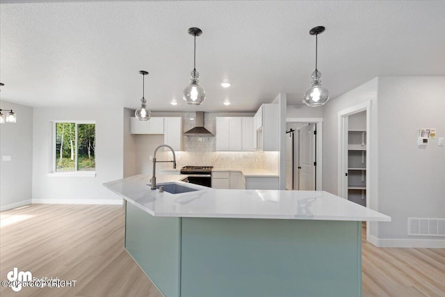 kitchen with sink, white cabinets, a large island, decorative backsplash, and wall chimney range hood