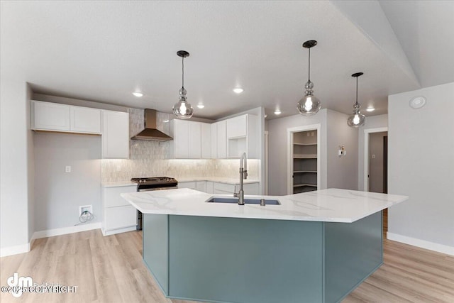 kitchen with gas range, an island with sink, wall chimney exhaust hood, and sink