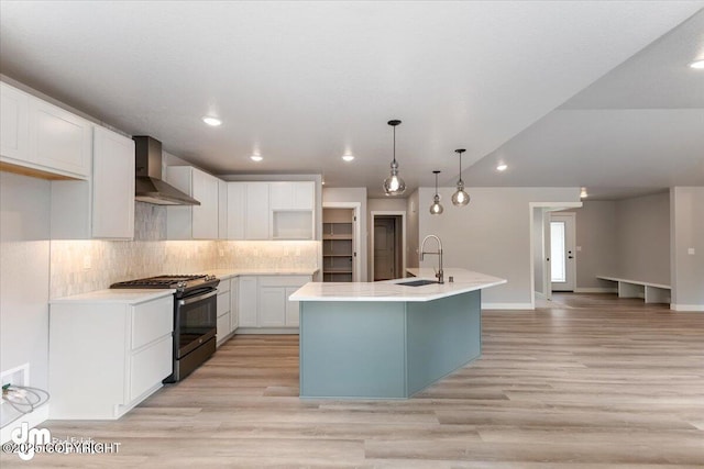 kitchen with white cabinets, stainless steel gas range, an island with sink, sink, and wall chimney range hood