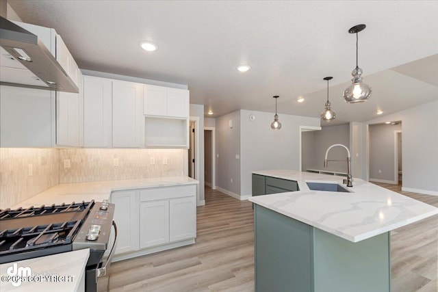 kitchen featuring stainless steel gas range, wall chimney range hood, a kitchen island with sink, white cabinetry, and sink