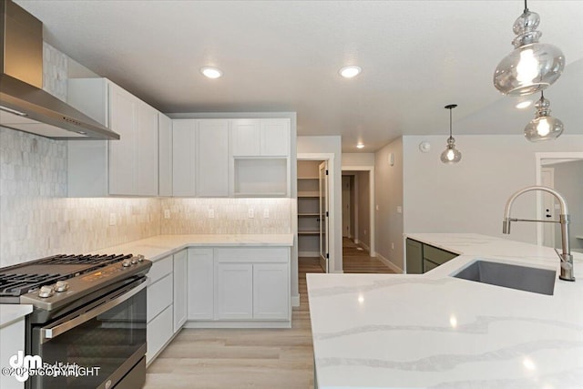 kitchen featuring white cabinets, wall chimney range hood, stainless steel range with gas cooktop, and sink