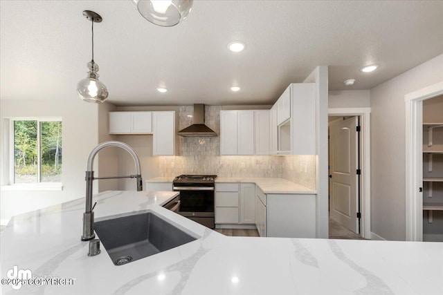 kitchen with light stone countertops, stainless steel range with gas cooktop, sink, white cabinetry, and wall chimney range hood