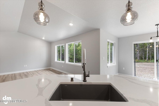 kitchen with light stone counters, a textured ceiling, vaulted ceiling, decorative light fixtures, and sink