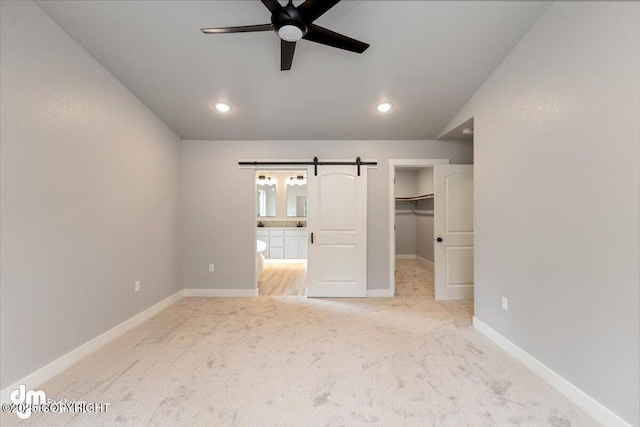 unfurnished bedroom with a closet, light colored carpet, ceiling fan, a walk in closet, and lofted ceiling