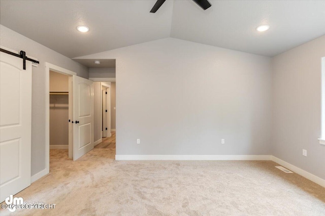 unfurnished bedroom featuring a spacious closet, a closet, lofted ceiling, a barn door, and ceiling fan