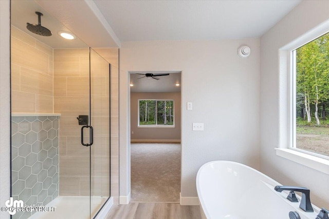 bathroom featuring ceiling fan, plus walk in shower, plenty of natural light, and wood-type flooring