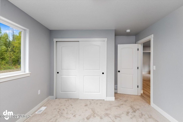 unfurnished bedroom with a textured ceiling, light carpet, a closet, and multiple windows