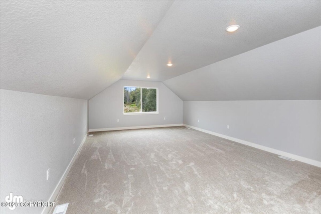 additional living space with a textured ceiling, light colored carpet, and lofted ceiling