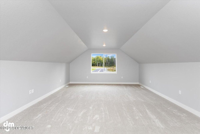 additional living space with a textured ceiling, vaulted ceiling, and light carpet