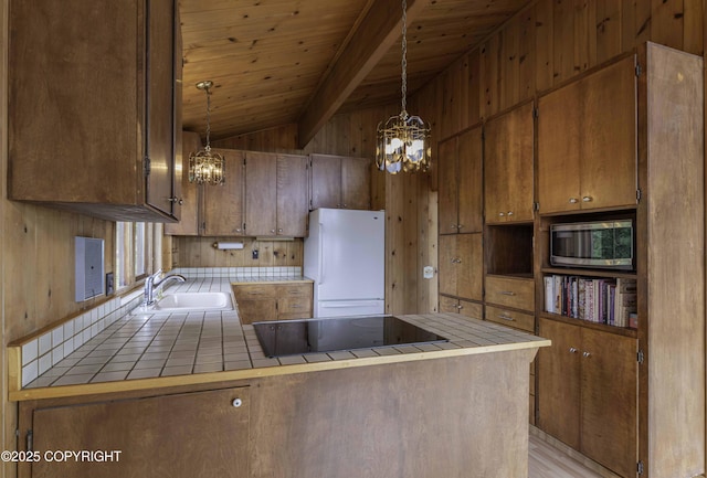 kitchen featuring black electric stovetop, white fridge, decorative light fixtures, and tile countertops