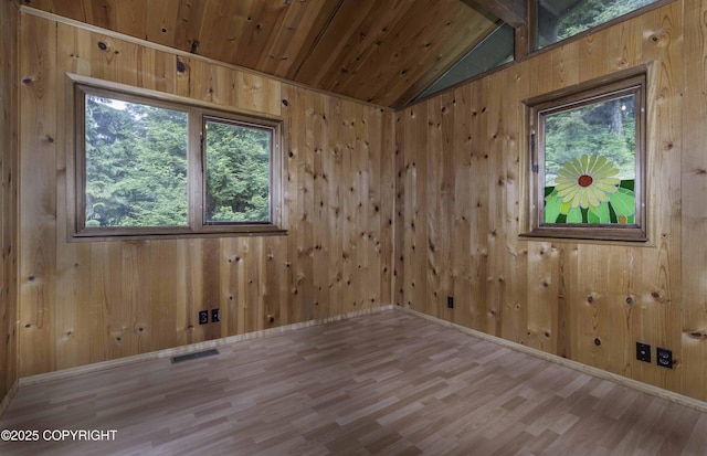 spare room featuring lofted ceiling, wood walls, light wood-type flooring, and a healthy amount of sunlight