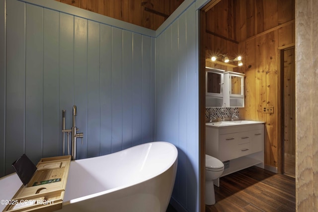 bathroom featuring toilet, hardwood / wood-style flooring, wooden walls, and vanity