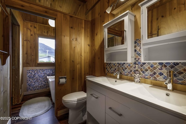 bathroom featuring toilet, vanity, wood walls, and backsplash