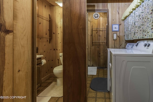 bathroom with toilet, wood walls, washing machine and clothes dryer, and vanity