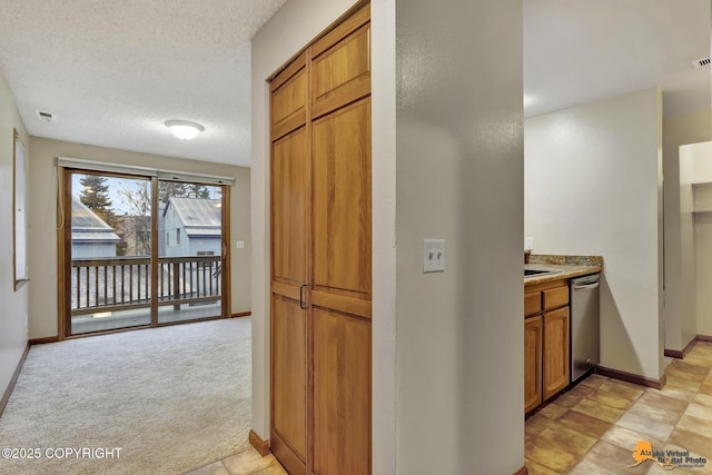 kitchen featuring a textured ceiling, dishwasher, and light colored carpet