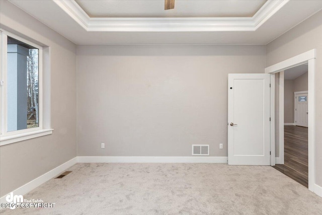 empty room with ornamental molding, light carpet, and a tray ceiling