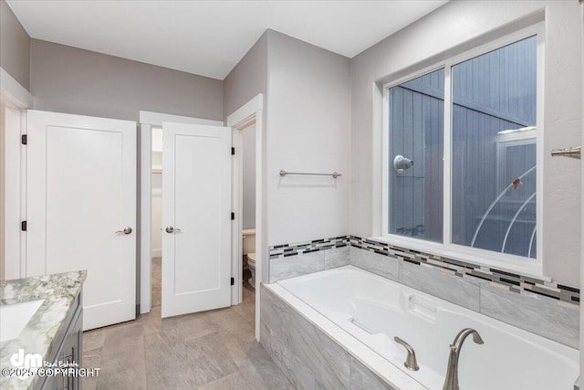 bathroom with vanity, tiled bath, and toilet