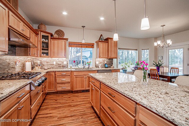 kitchen featuring sink, tasteful backsplash, light wood-type flooring, pendant lighting, and light stone countertops