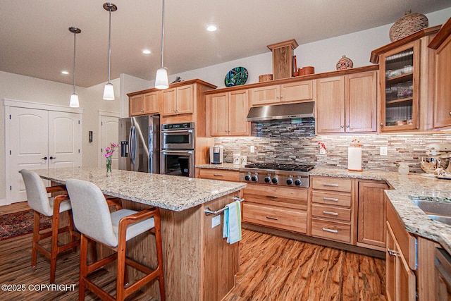 kitchen featuring light stone counters, decorative light fixtures, a kitchen island, stainless steel appliances, and decorative backsplash