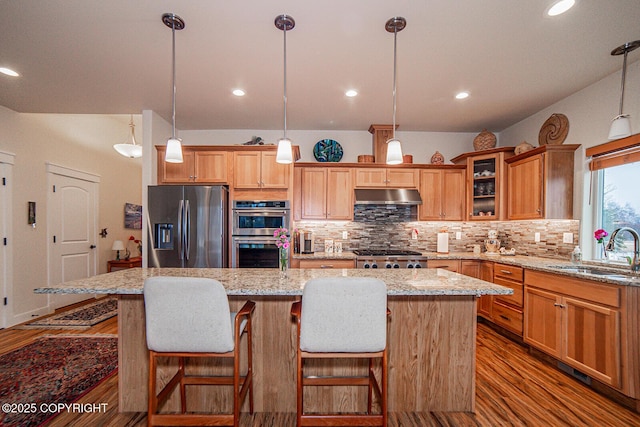 kitchen with a kitchen island, appliances with stainless steel finishes, sink, hardwood / wood-style flooring, and hanging light fixtures