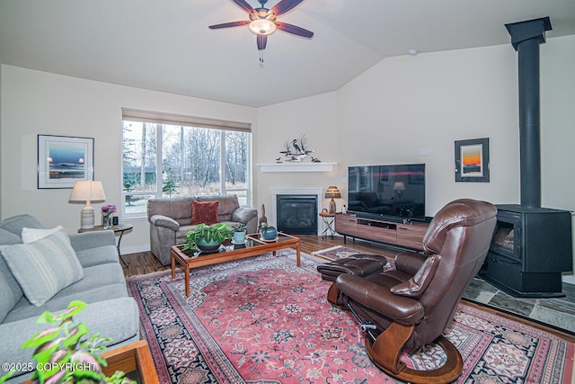 living room featuring ceiling fan, a fireplace, wood-type flooring, vaulted ceiling, and a wood stove