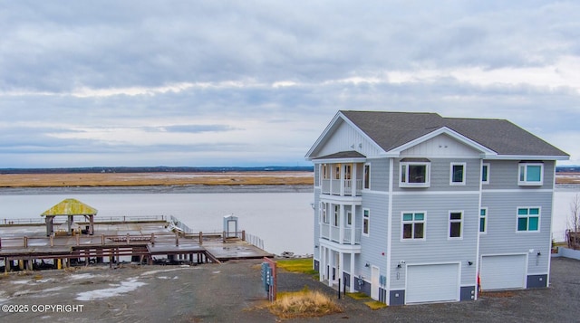 exterior space featuring roof with shingles, a water view, an attached garage, board and batten siding, and driveway