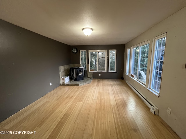 unfurnished living room featuring baseboard heating, a wood stove, and hardwood / wood-style flooring