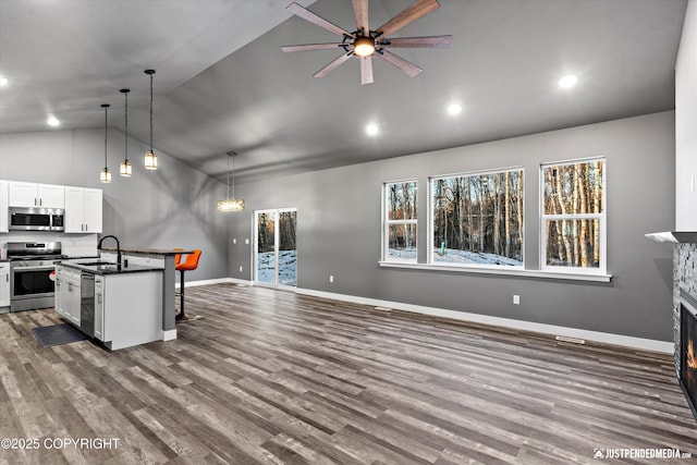 kitchen with decorative light fixtures, white cabinetry, stainless steel appliances, an island with sink, and sink