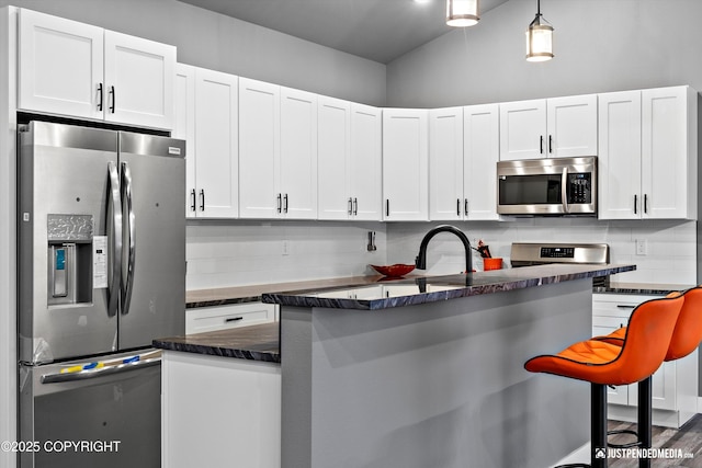 kitchen featuring appliances with stainless steel finishes, white cabinets, decorative light fixtures, backsplash, and a breakfast bar