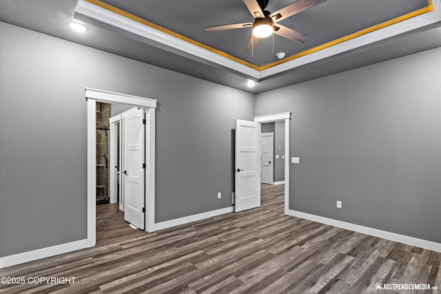 unfurnished bedroom with ceiling fan, ornamental molding, dark hardwood / wood-style floors, and a tray ceiling