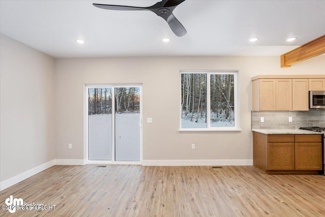 kitchen with tasteful backsplash, ceiling fan, appliances with stainless steel finishes, and light hardwood / wood-style flooring