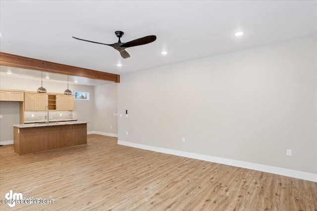 unfurnished living room with ceiling fan, sink, beamed ceiling, and light wood-type flooring