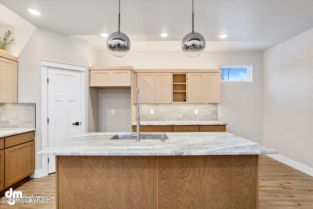 kitchen featuring light stone counters, sink, and an island with sink