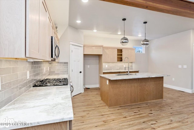 kitchen with an island with sink, sink, light brown cabinetry, and decorative light fixtures