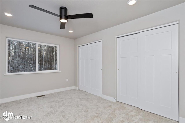 unfurnished bedroom with ceiling fan, light carpet, and two closets