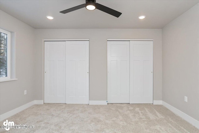 unfurnished bedroom featuring multiple closets, ceiling fan, and light carpet